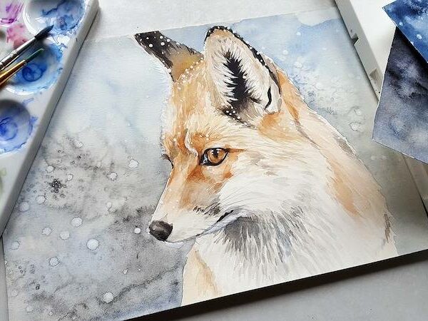 Artist using watercolors to paint a fox in winter snow on textured paper.