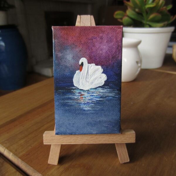 Person painting a swan on a small stretched canvas during a guided art class.