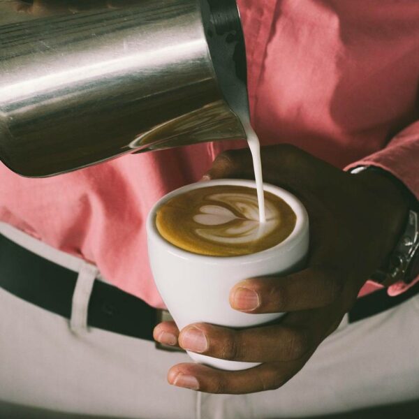 Barista pouring steamed milk into a cup of espresso to create a latte art heart design.
