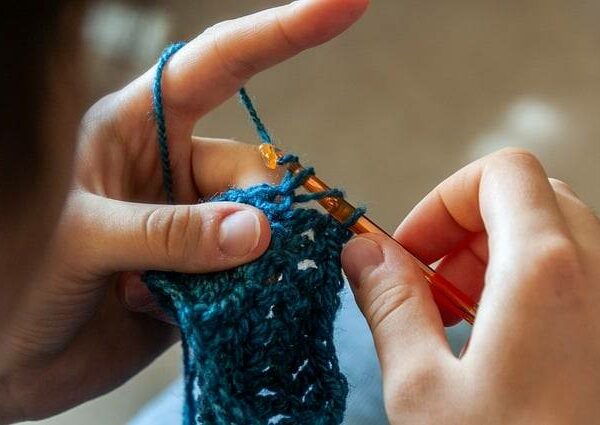 Close-up of hands crocheting a blue scarf during a beginner-friendly crochet class.
